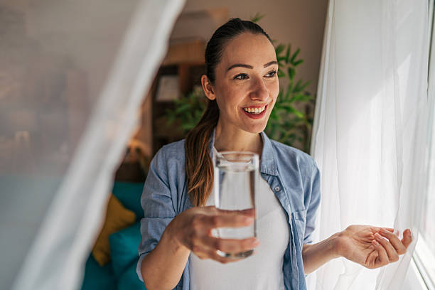 istock Young woman drinking water and looking out the window 2208793400