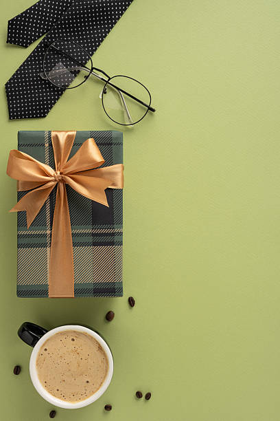 istock Gift box, cup of coffee, eyeglasses, and tie displayed against a vertical green surface 2208807179
