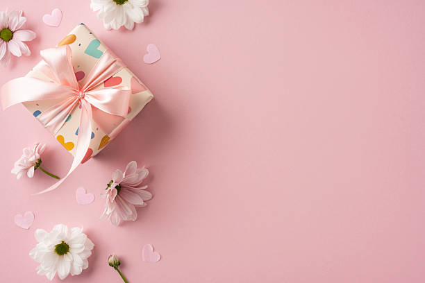 istock A charming gift box wrapped with pink ribbon, accompanied by daisies scattered elegantly on a soft pink background, evoking a celebratory and cheerful mood 2208807203