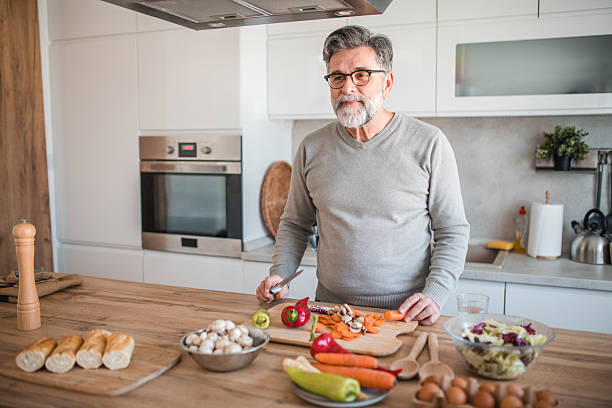 istock A smiling senior man stands at the kitchen counter while making an organic salad 2208810902