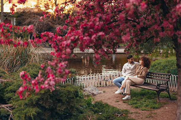 istock Couple relaxing on bench under blooming tree by lake in park 2208811177