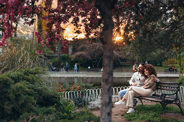 istock Young couple relaxing on bench in park at sunset 2208811217