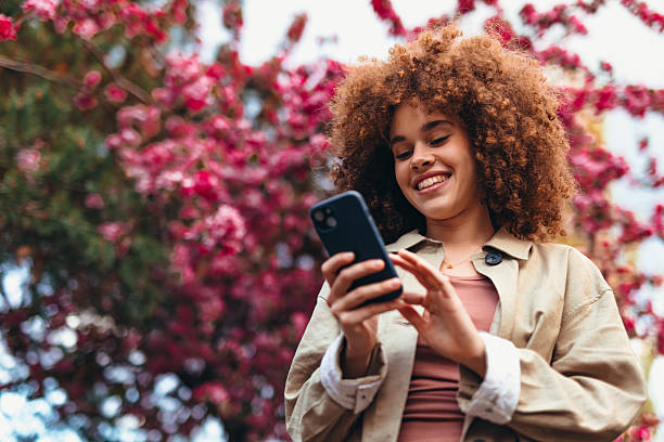 Young woman using smartphone in front of blooming tree in spring