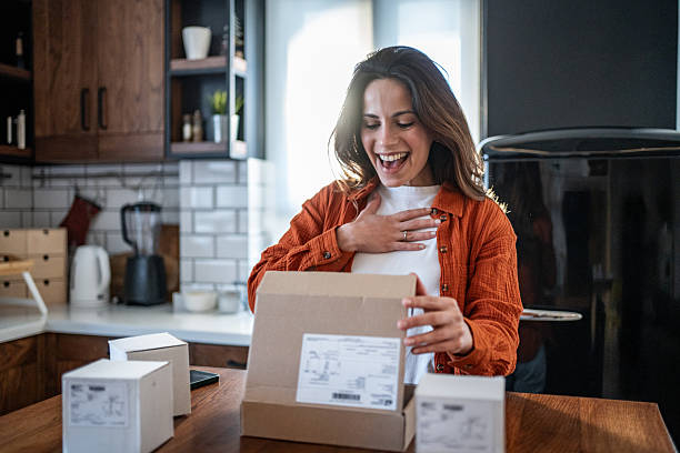 istock Excited woman opening parcel at home in the kitchen 2208822582
