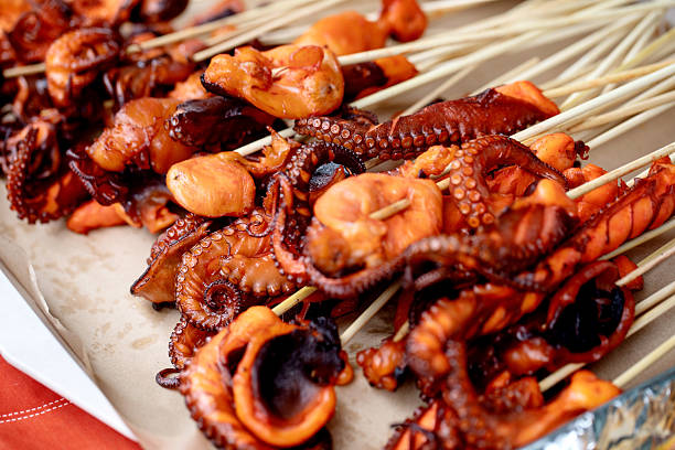 Closeup of grilled baby octopus on wooden skewers. Seafood barbecue with charred octopus pieces showcasing tentacles texture. Mediterranean cuisine street food.