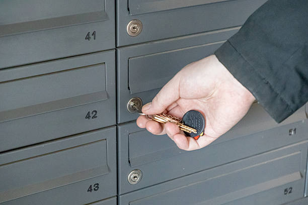 Hand with keys unlocking numbered mailbox in residential building lobby closeup view of keyhole and mail slots