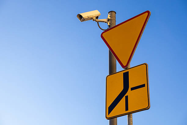 istock surveillance camera and road signs showing intersection priority under blue sky with sunlight warning drivers about merging traffic and monitoring system ahead 2208845038
