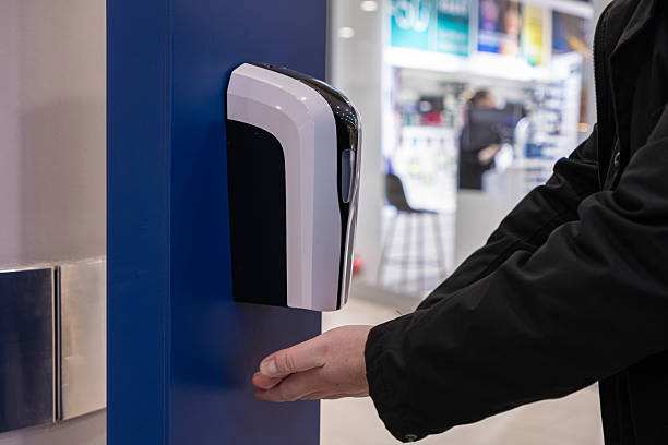 istock Person using automatic hand sanitizer dispenser in shopping mall, placing hand under sensor for hygienic gel application in public indoor space 2208845166