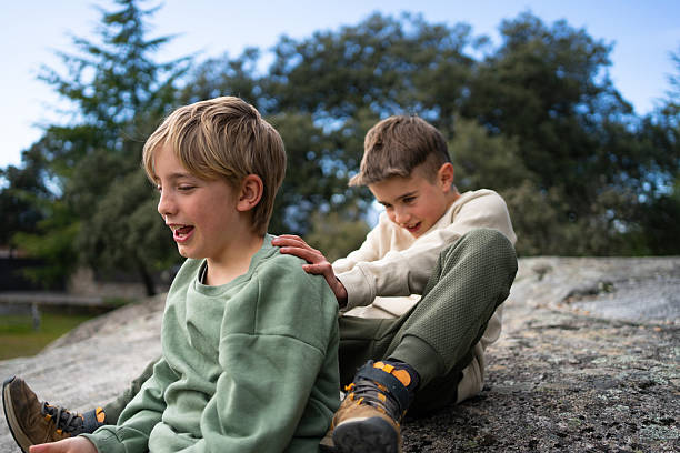 Two brothers are sitting on a large rock, playing and laughing together in nature
