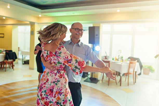 Mature couple dancing together in an elegant event space. The woman wears a colorful floral dress, while her partner is dressed in a light blue shirt, both fully immersed in the rhythm and joy of the celebration. \nShot with Canon R5