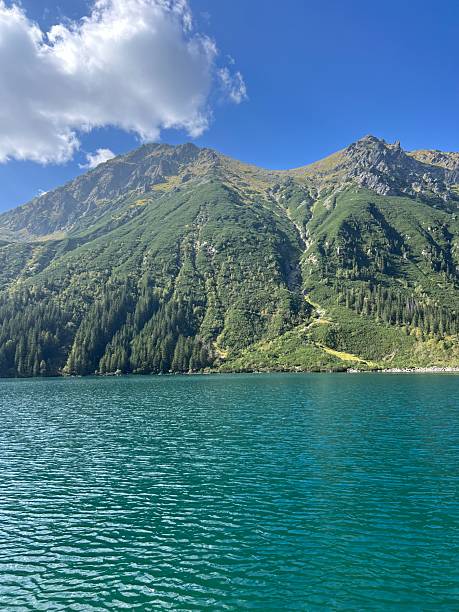 istock Clear alpine lake mirrors lush green slopes under crisp blue sky 2208850899