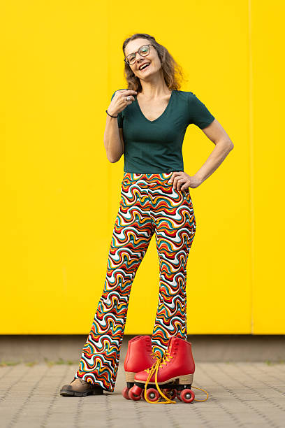 Portrait of mature woman against yellow wall in urban area. She is holding roll shoes and she looks very happy