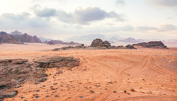istock Orange red sand desert, rocky formations and mountains background, overcast sky above, camp tents visible at distance - typical scenery in Wadi Rum, Jordan 2208856144