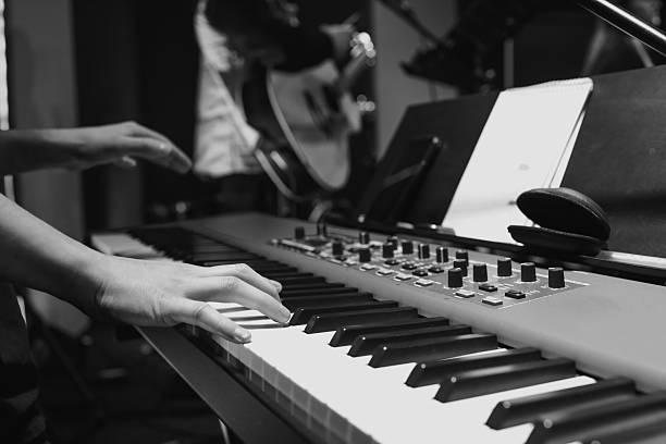 istock Musician's hands playing a keyboard during worship practice, with a guitarist blurred in the background. Black and white image captures emotion and focus 2208858533