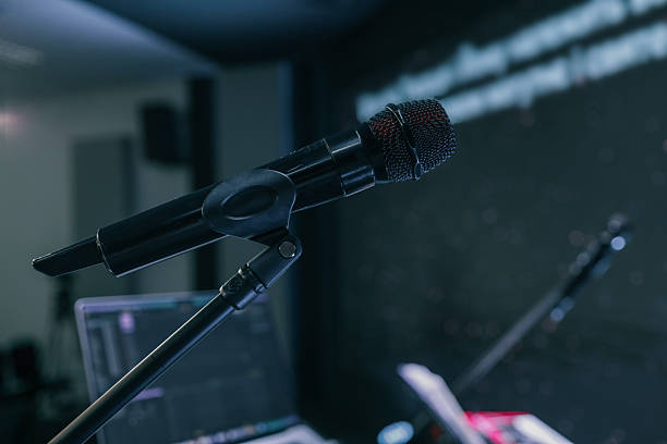 istock Close-up of a microphone on a stand in a dimly lit studio or stage with blurred background and a laptop screen visible 2208858540