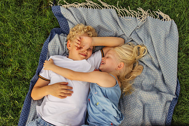 A five-year-old Eurasian girl sits in the grass with her younger brother as they collect and share candy from a piñata during the girl's backyard birthday party.