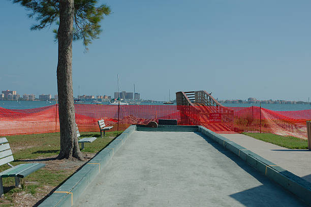 Section of beach and water cordoned off with a bright orange safety fence. Wide view looking out over Gulfport, FL beach. Section of beach and water cordoned off with a bright orange safety fence. Broken wooden boardwalk bridge extends over waterway. Sky is clear and blue during environmental beach nourishment restoration project near the coast. Background across the water cityscape of buildings is visible. gulfport florida photos stock pictures, royalty-free photos & images