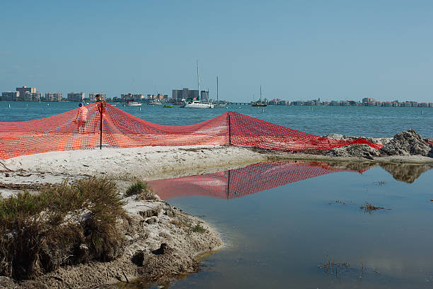 Section of beach and water cordoned off with a bright orange safety fence. Wide view looking out over Gulfport, FL beach. Section of beach and water cordoned off with a bright orange safety fence. Sky is clear and blue during environmental beach nourishment restoration project near the coast. Background across the water cityscape of buildings is visible. gulfport florida photos stock pictures, royalty-free photos & images