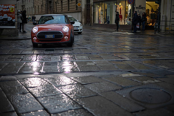 Turin, Italy - Nov 08 2021: A red Mini Cooper parked on a wet cobblestone street near a white Fiat