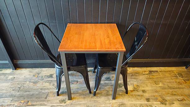 istock Small square wooden table with two black metal chairs against a dark paneled wall on a rustic wooden floor. 2208872027