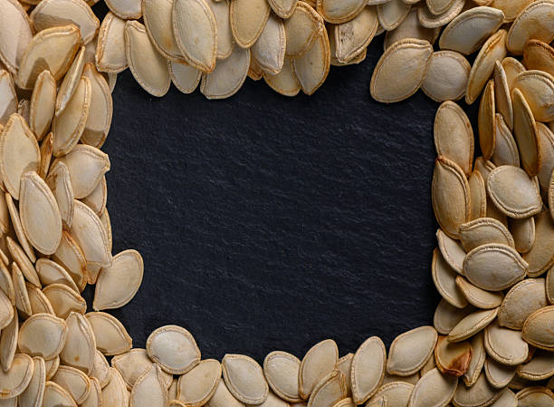 Pumpkin seeds arranged in a decorative frame on a dark slate background for autumnal culinary inspiration