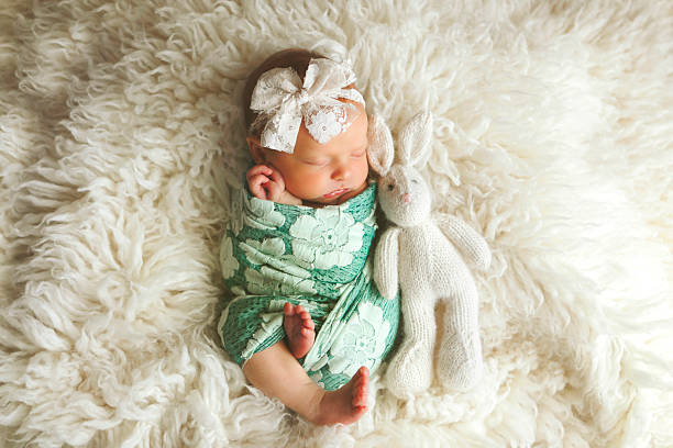 A newborn baby girl sleeping on sheep's wool, beside her knitted bunny stuffy. Shot with a Canon 5D Mark IV.