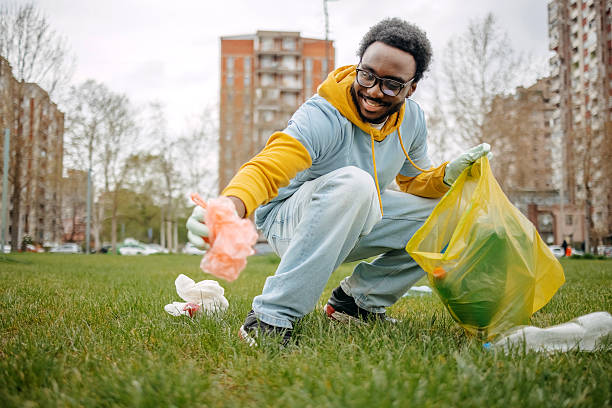 Young black volunteer in public park collecting garbage in plastic bag