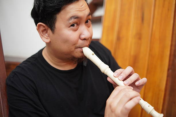 Young adult Asian man playing recorder flute, musical instrument