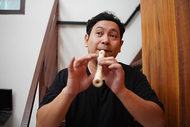 Young adult Asian man playing recorder flute, musical instrument