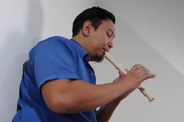 Young adult Asian man playing recorder flute, musical instrument