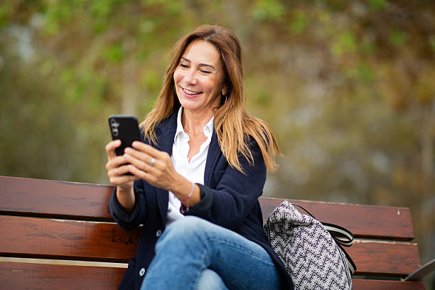 istock Relaxing on a park bench, a woman smiles as she scrolls through her phone 2208897872
