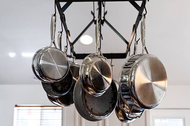 Pots and Pans Detail Hanging in Home Kitchen - Cooking pots and sauté pans hanging in center of kitchen. Bright interior setting.