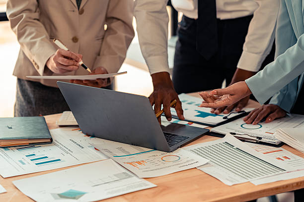 istock Paperwork and hands on table in business presentation or seminar Group of confident businessmen pointing at graphs and charts to analyze market data, balance sheet, accounting, net profit. 2208916395