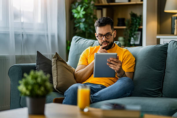 istock Man relaxing at home and watching podcasts on digital tablet at home. 2208918530