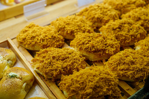 Close-up of golden brown buns topped with chicken floss, neatly arranged on a wooden tray in a local bakery.