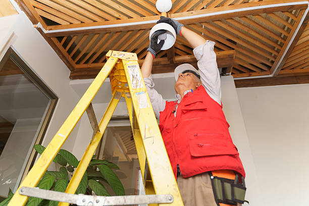 Latin american senior electrician working on a ladder, changing a ceiling light fixture