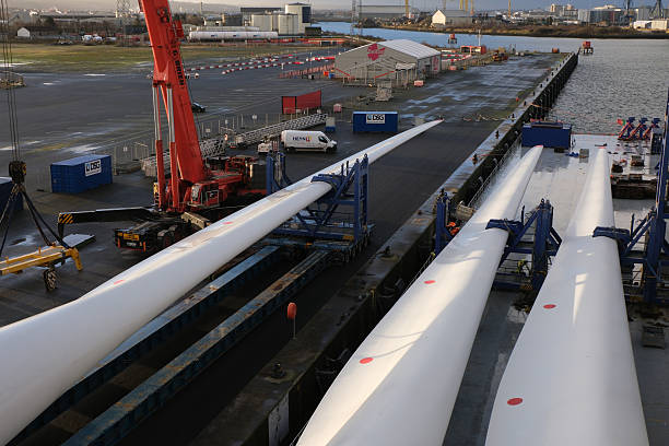 Belfast, UK - 12 19 2024: Blade of wind turbine secured on self propelled modular trailer ready for loading by mobile cranes on the heavy load carrier vessel in port of Belfast.