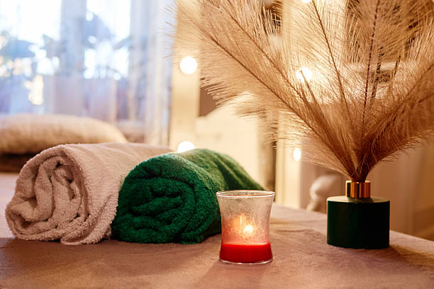 A serene spa environment showcases neatly rolled towels in green and white alongside a lit candle and decorative plant. Soft lighting enhances the peaceful ambiance for relaxation