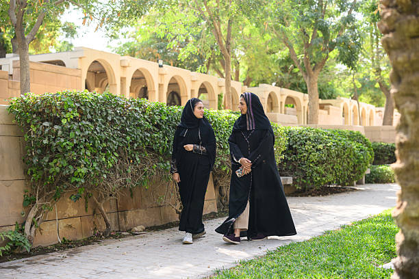 istock Two hijabi friends chatting and walking through a lush green park 2208933765