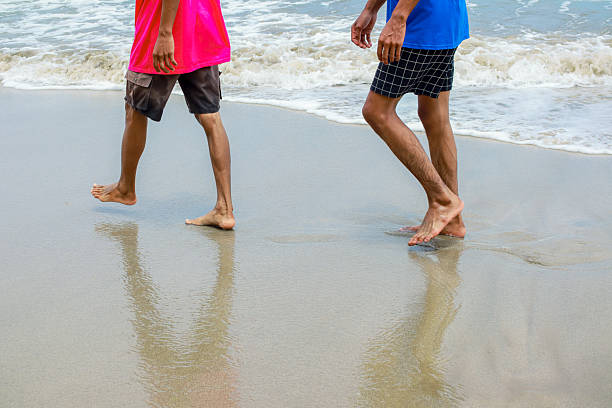 istock Barefoot Stroll: Two Individuals Walking on a Sandy Beach Along the Shoreline 2208934743