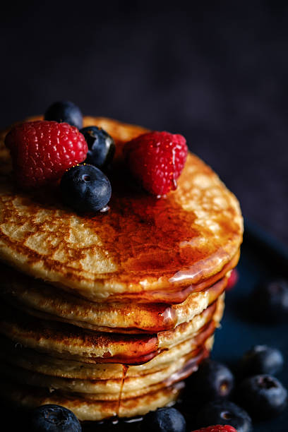 istock Stacked pancakes with raspberries and blueberries and maple syrup against a dark background. 2208935638