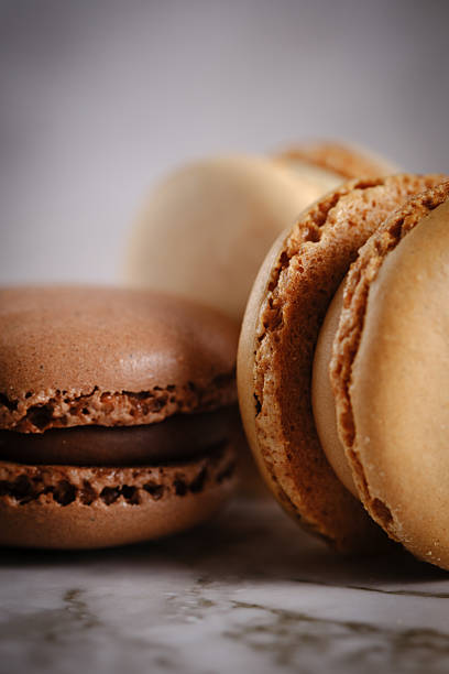 Vertical close up of 3 brown toned macaroons against a light background. French macaron. Food photography.