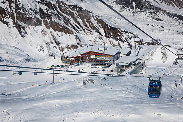 Hintertux, Austria - March 03, 2025: Ski slope and overhead cable car at the hintertux glacier in the Zillertal Alps in Austria. A huge mountain restaurant and the cable car station with many people around.