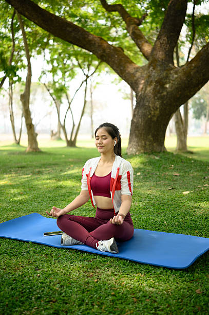 istock Young woman practicing meditation outdoors on mat under the shade of trees 2208940109