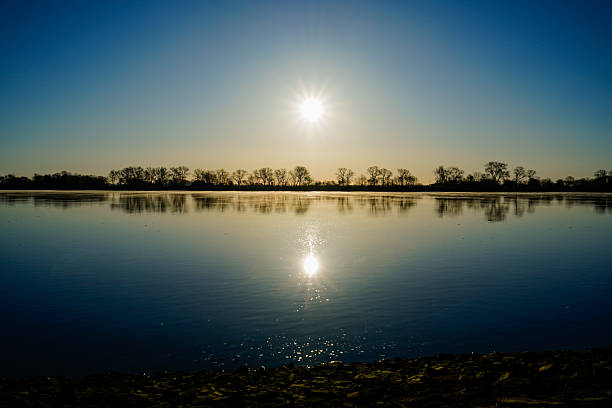 The sunrise is reflected in the calm river, surrounded by bare trees, Weserstrand 26931 Oberhammelwarden-Germany