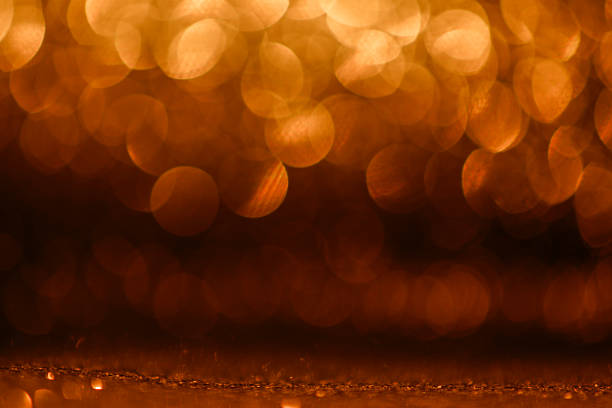 Fancy orange color glitter sparkle background. Defocused orange color sequin light. Fancy orange color glitter sparkle background. Studio shooting of a creative bright orange color background. It is textured color gradient. There are no text and no people, and have copy space for design. Its Suitable for commercial use. Christmas, New Year, Diwali festive celebrations themed backgrounds, wallpapers, templates for greeting cards, banners and posters and wrapping paper is apt.