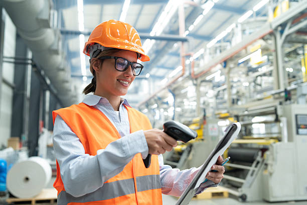istock Smiling woman in safety gear scans document with barcode scanner in factory setting. 2208944867