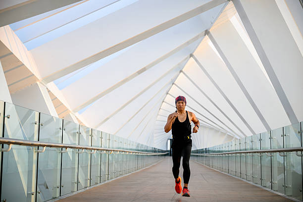 Full length shot of a runner in motion on a pedestrian bridge with a geometric design. Man doing fitness training across modern architecture in Dubai.