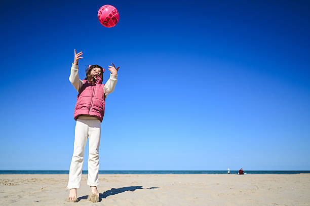 istock Young girl playing with pink ball on sandy beach 2208948023