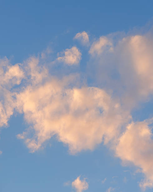 Soft pastel clouds illuminated by the warm evening sun against a clear blue sky